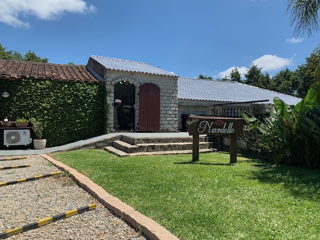 parte externa da vinícola, com uma plaquinha, grama e porta de entrada