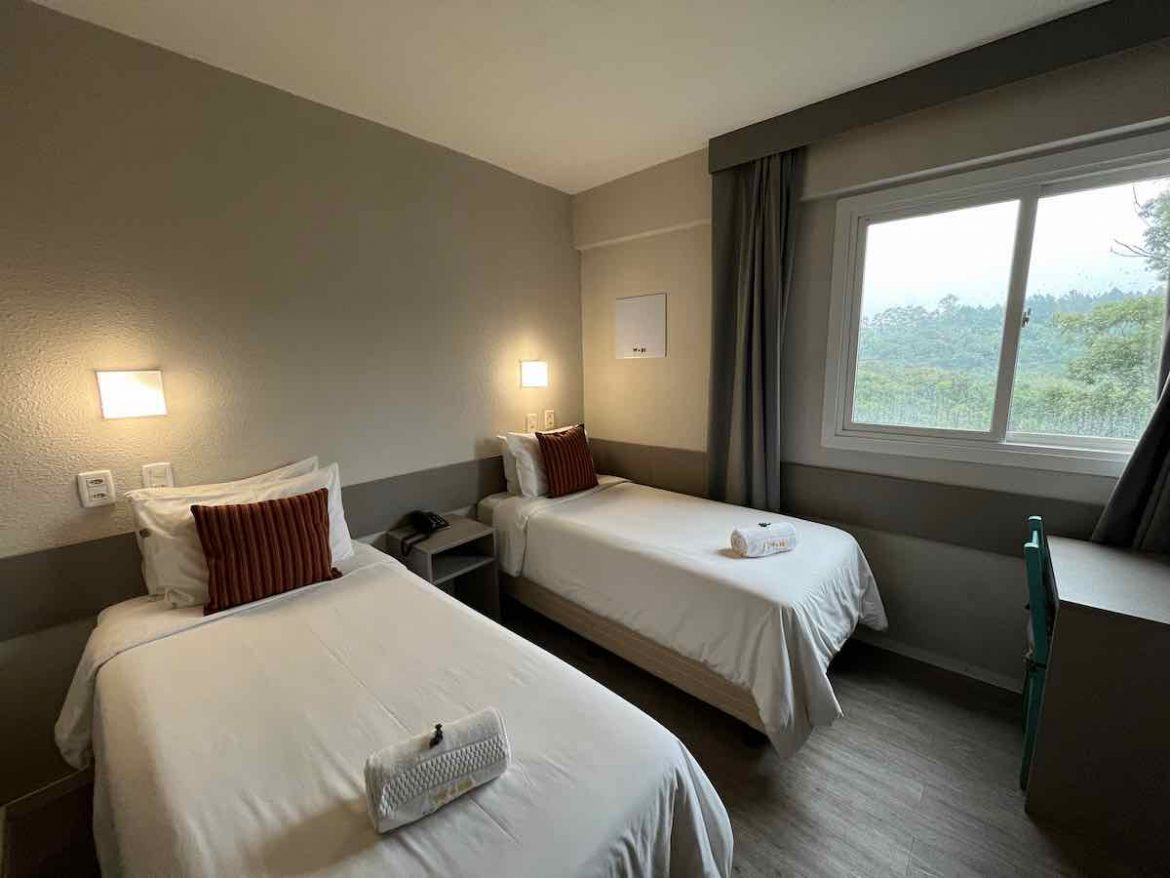 O que fazer em São Leopoldo: na foto duas camas com cobertas claras e almofadas na cor vinho