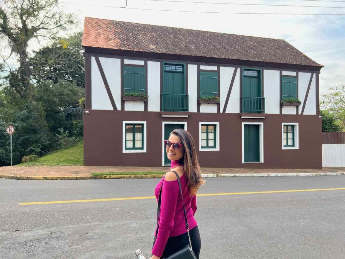 O que fazer em Novo Hamburgo: na foto a jornalista Anelise Zanoni posa em frente a uma casinha enxaimel
