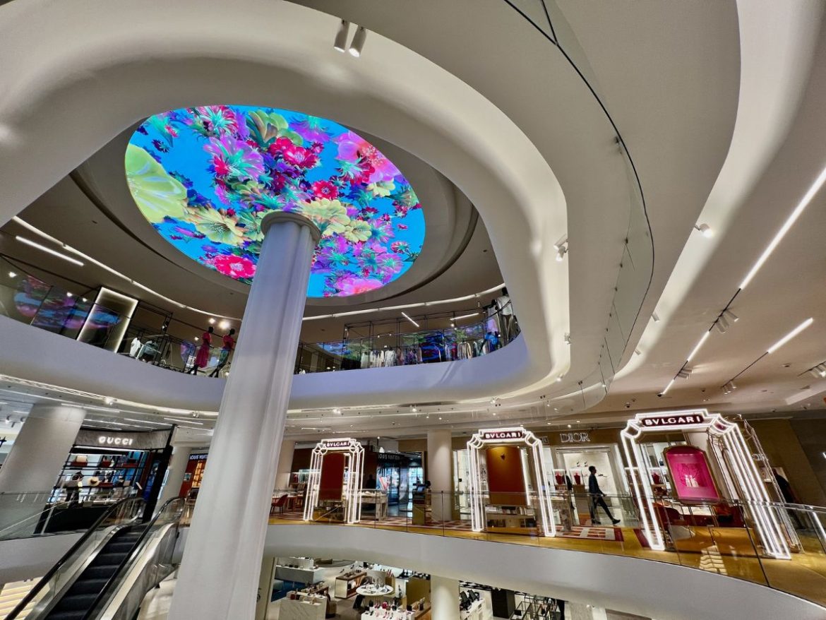 O que fazer em Madri: na foto aparece o teto iluminado do el corte ingles, com uma vidraça colorida acompanha de uma coluna que vai até o chão e diversas lojas em volta
